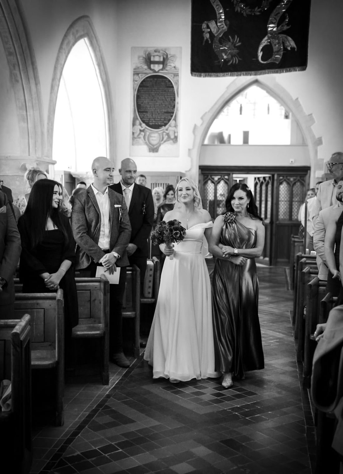 Bride walking down the church aisle with her mother, in black and white
