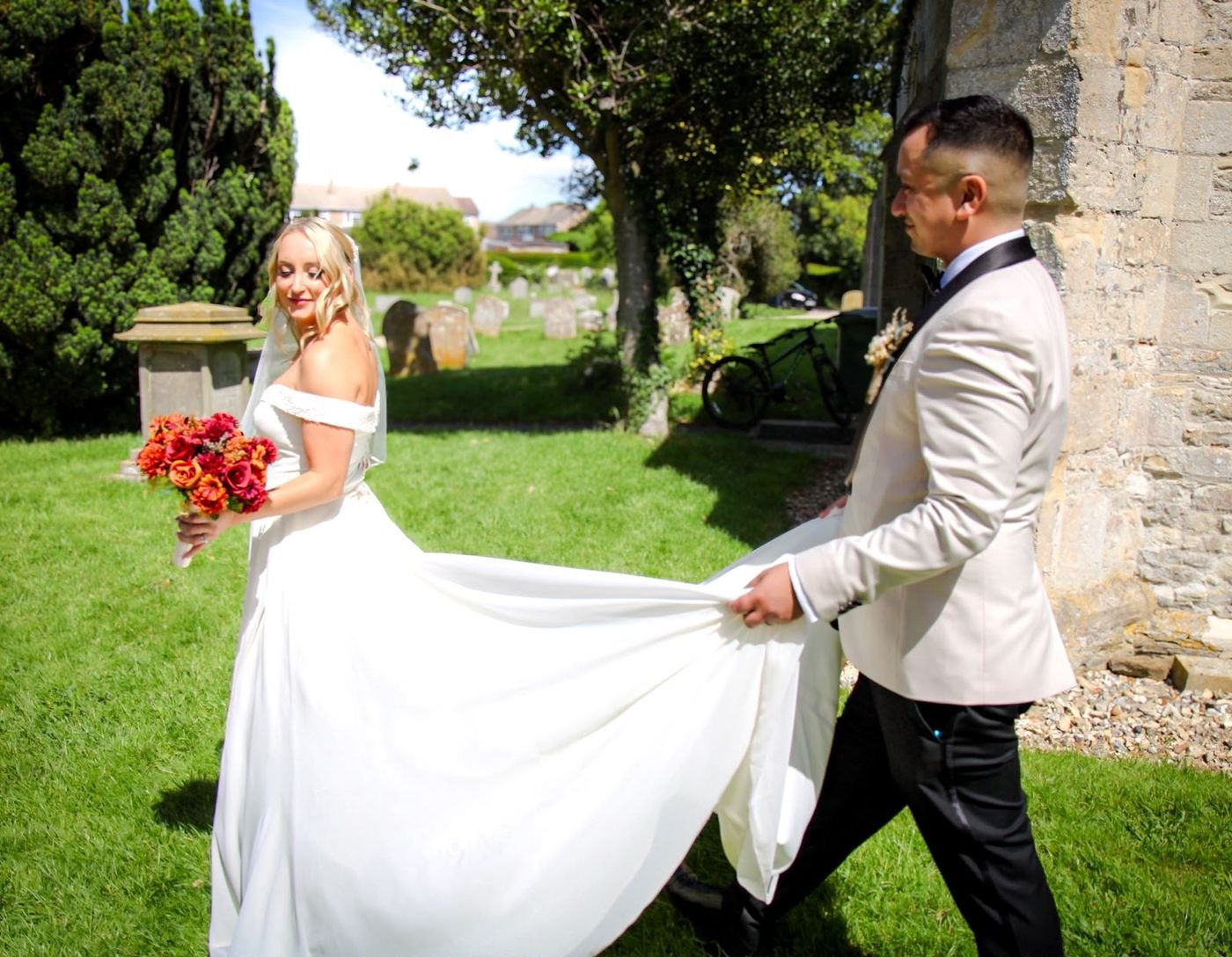 Groom carrying the bride's train through the churchyard
