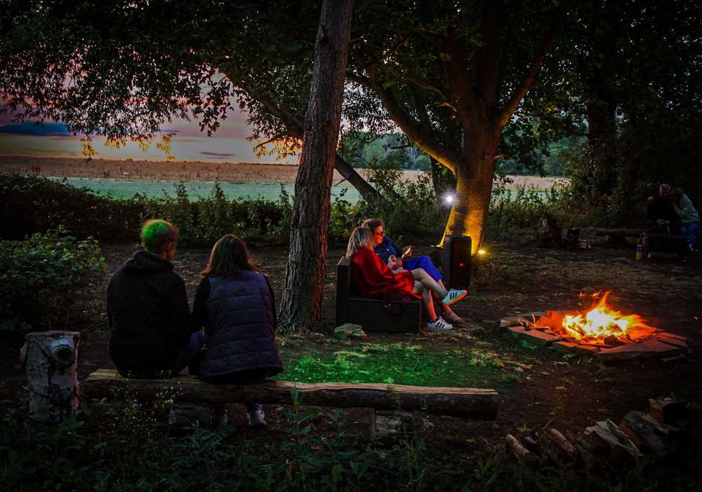 Friends gathered around a campfire at dusk beside an Oxfordshire field