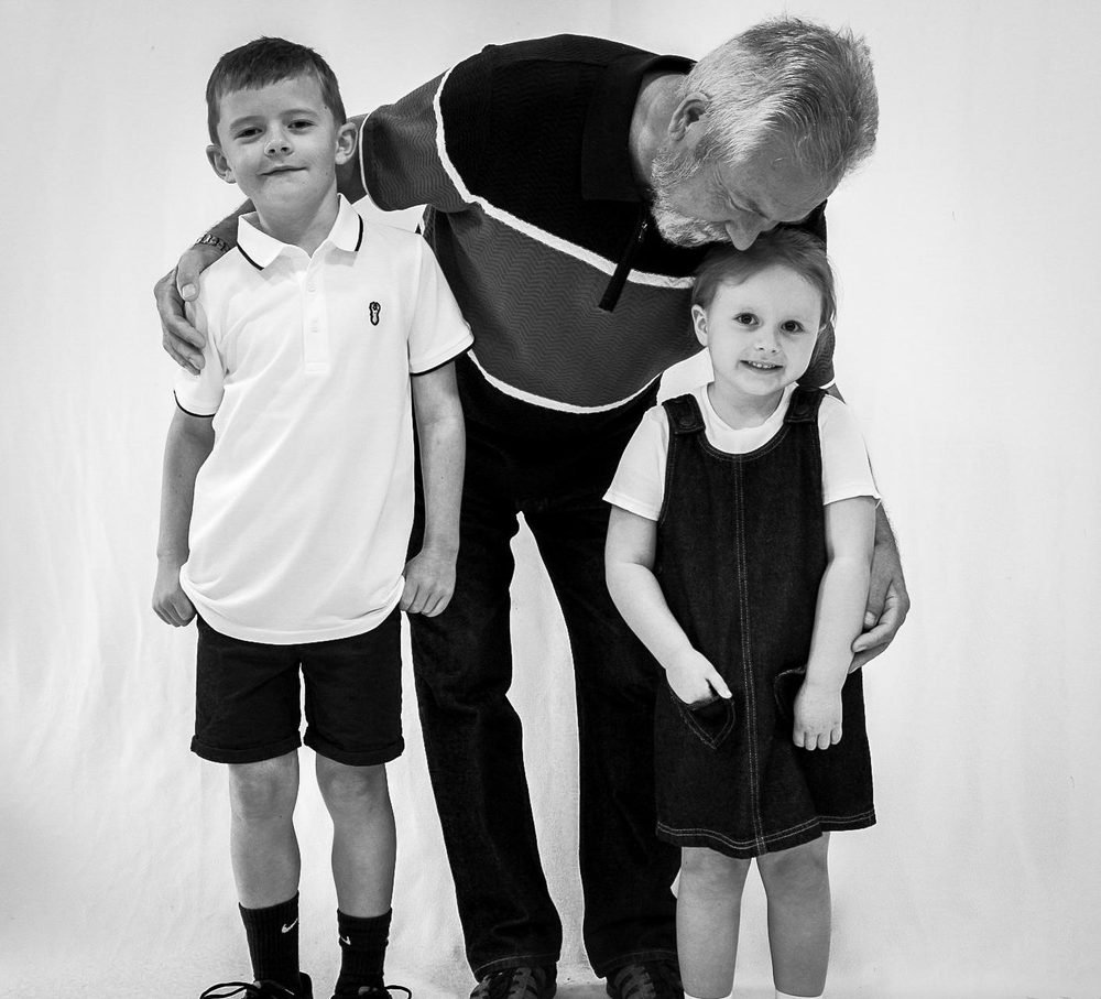 Grandad kissing his granddaughter's head during a studio family shoot, in black and white
