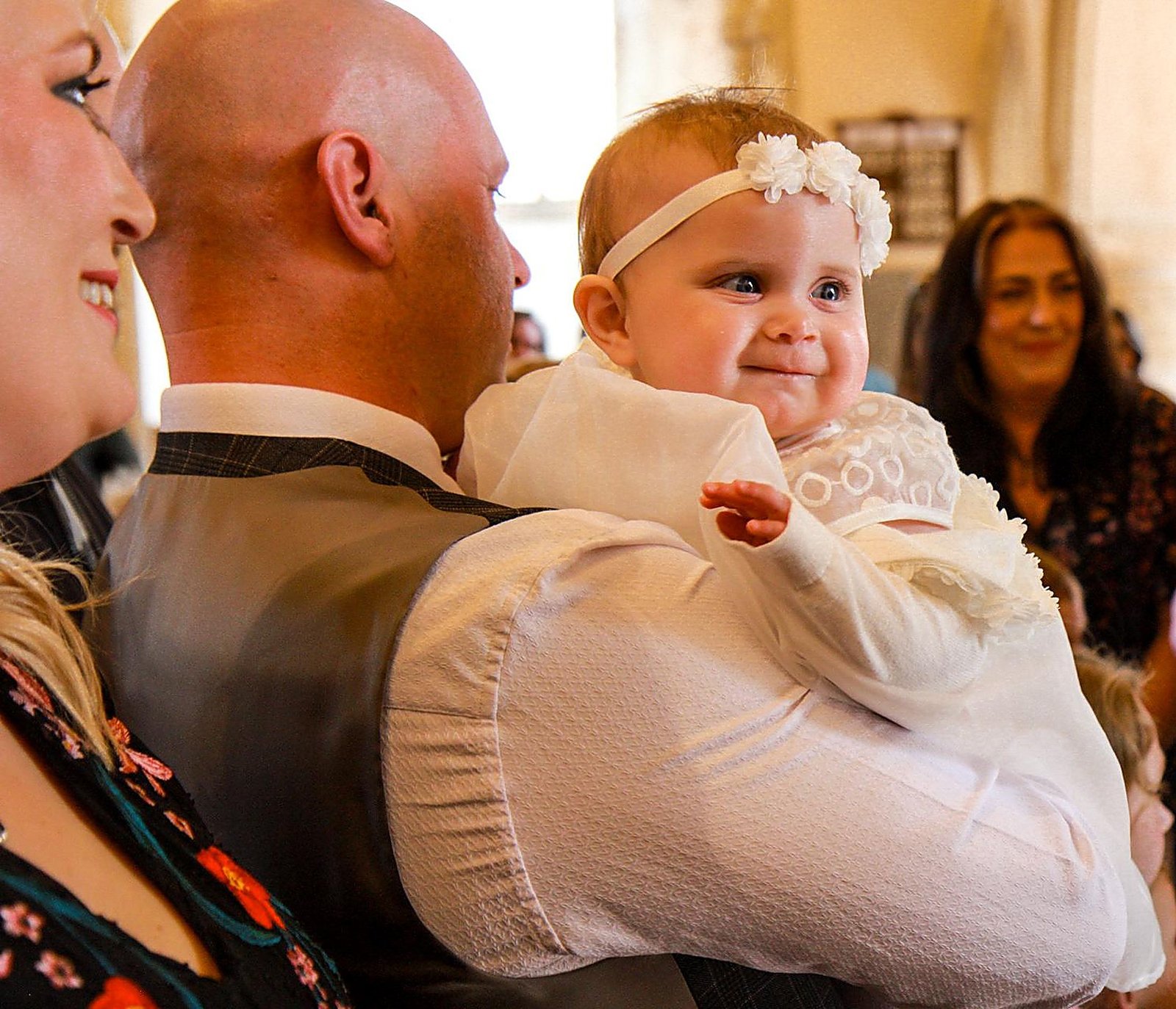 Baby in a christening gown smiling over her father's shoulder