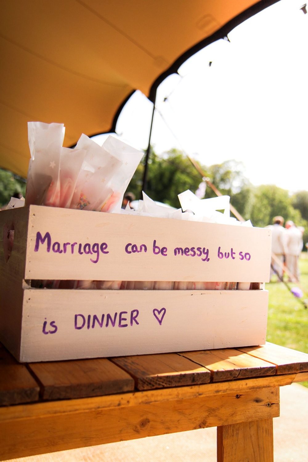 Crate of sweet bags with a hand-written marriage joke at an outdoor reception
