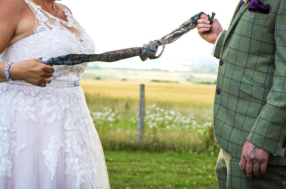 Handfasting ribbon between bride and groom overlooking the fields