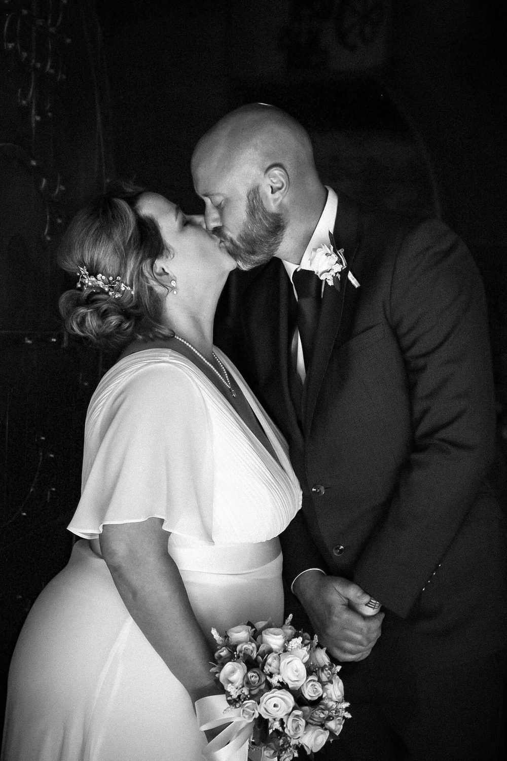 Newlyweds kissing in the church doorway, in black and white