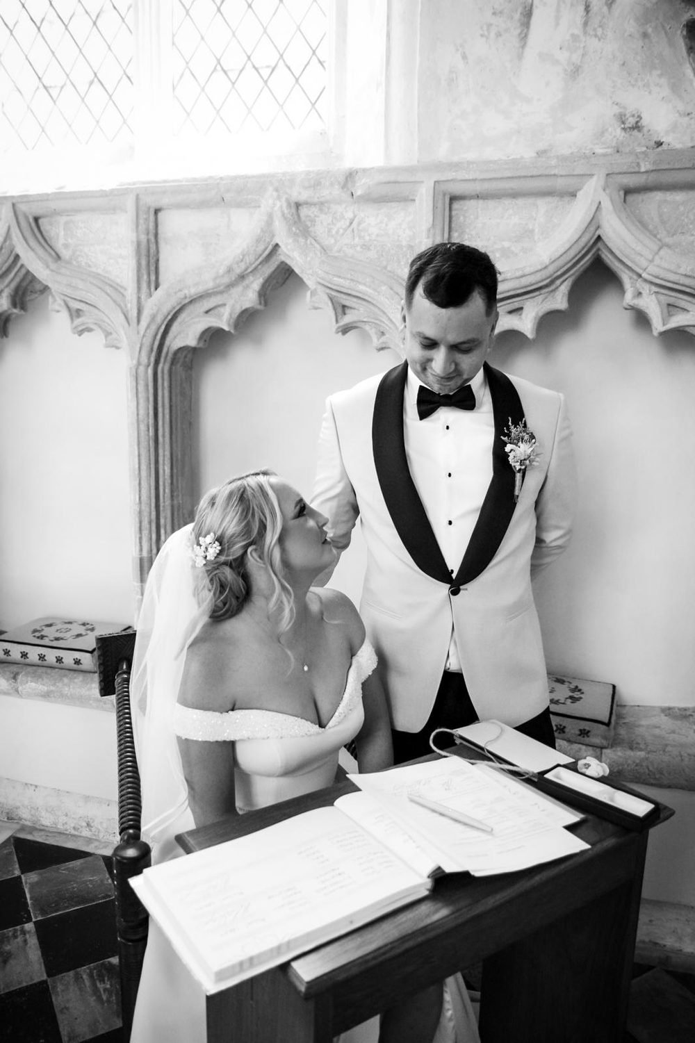 Bride and groom sharing a look while signing the register, in black and white