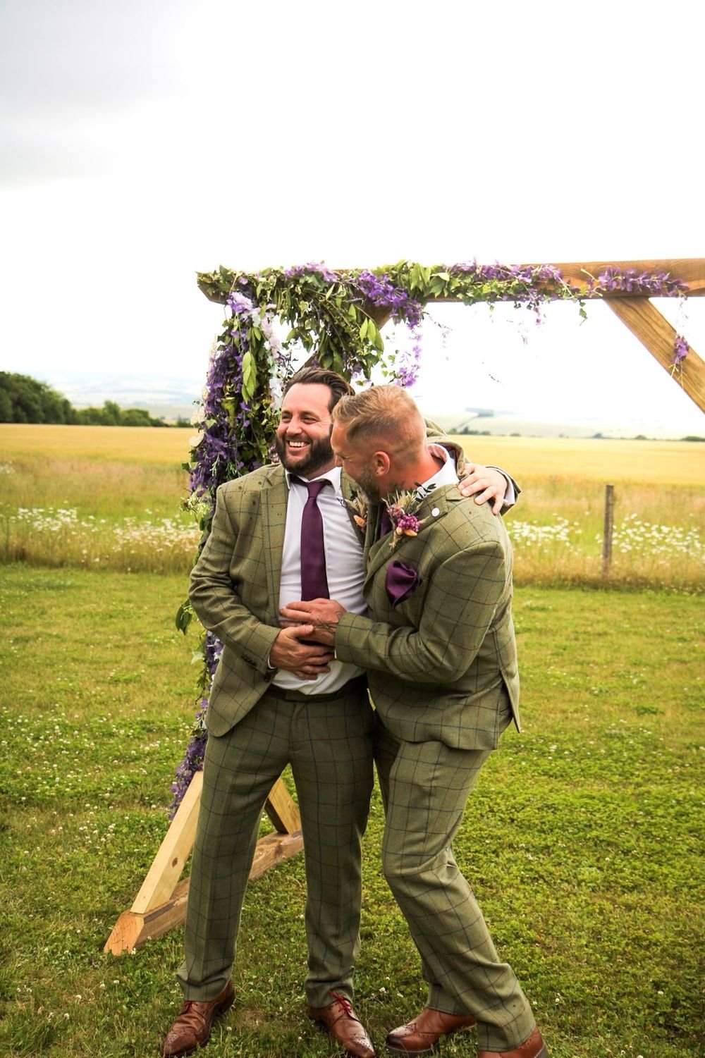 Groom and best man laughing by the flower-covered arch