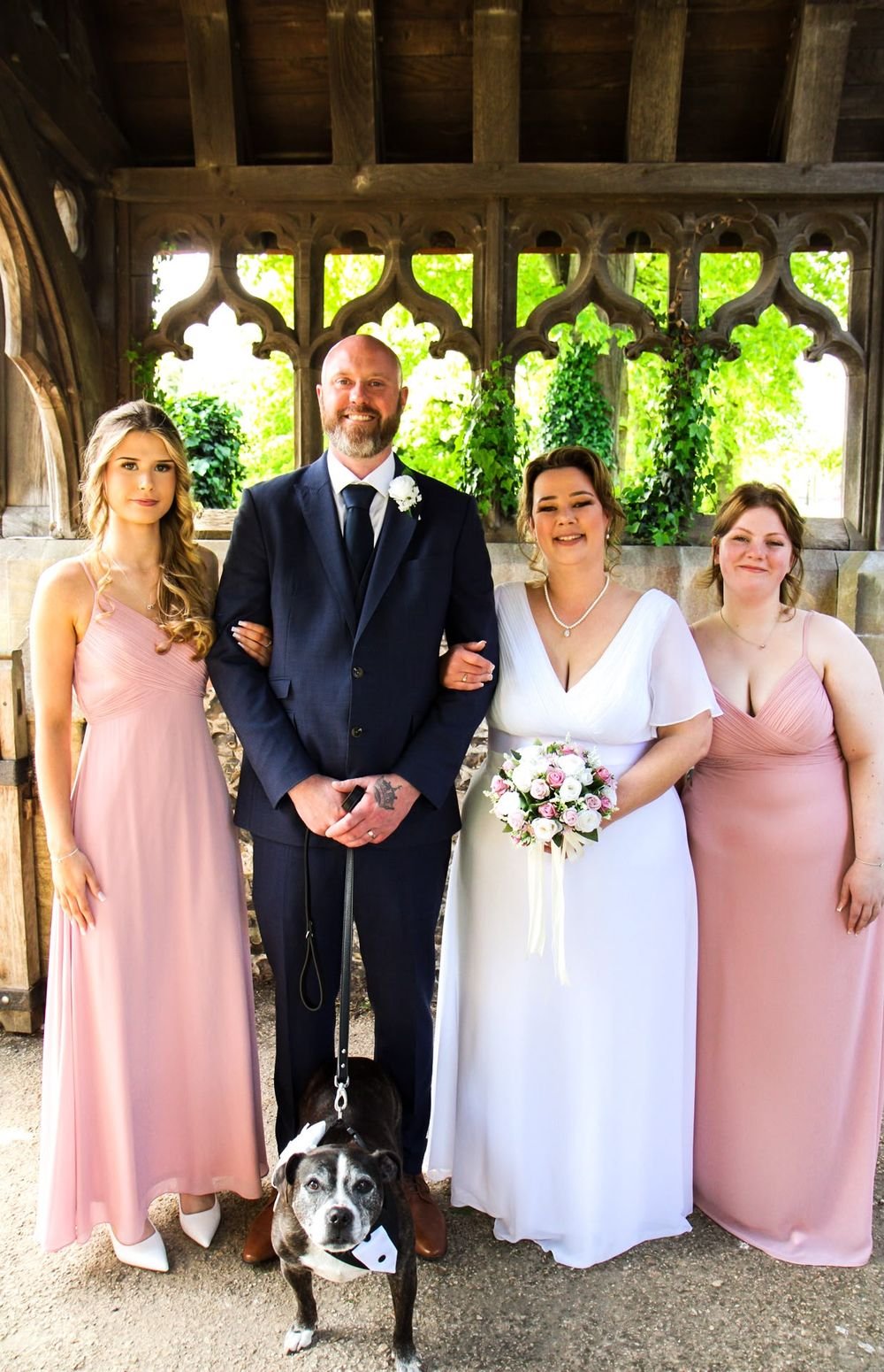 Bride and groom with bridesmaids and their dog in a tuxedo bandana